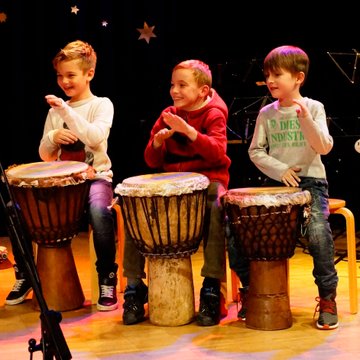 Drei Jungen spielen lachend auf afrikanische Trommeln