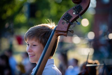 Junge mit Kontrabass, im Freien, die Sonne scheint