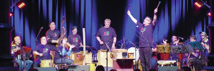 Ensemble mit verschiedenen Orff-Instrumenten. In der Mitte ein Mann, der beide Arme nach oben streckt. Alle tragen das Festival-T-Shirt FIS 2013