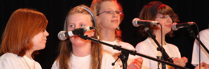 Vier Mädchen in weißen T-Shirts singen, vor ihnen stehen MikrosMusikschule Fürth