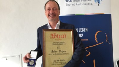 Robert Wagner freudig mit Carl-Orff-Medaille und dazugehöriger Urkunde in den Händen